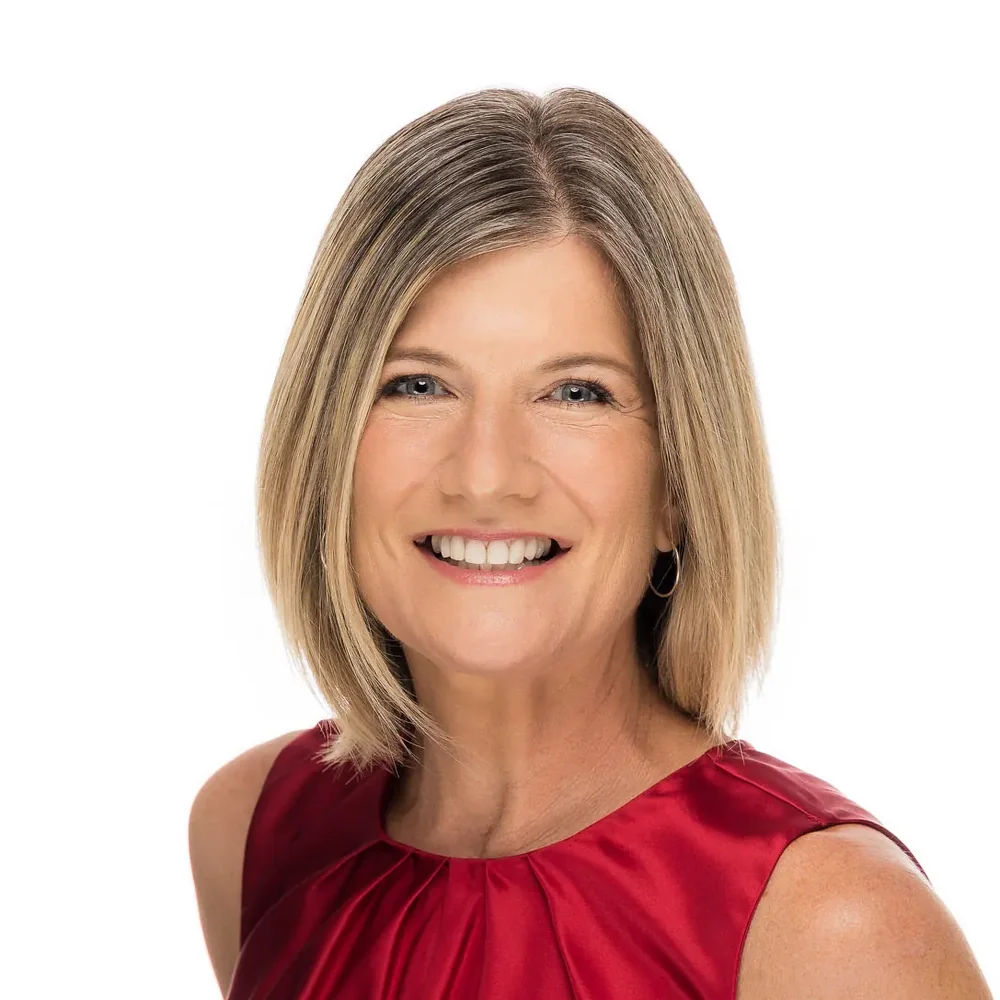 Professional headshot of a woman in a red satin top with a wide smile on a white backdrop