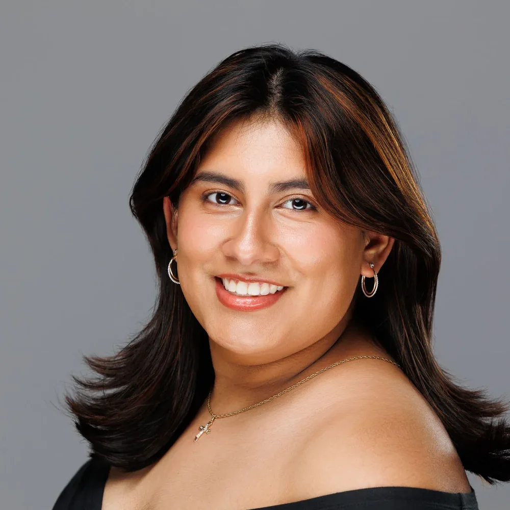 Individual headshot of a woman in a black off-shoulder top on a gray backdrop