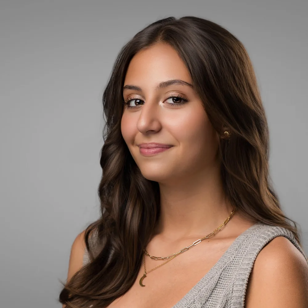 Studio headshot of a young woman with long dark hair in a soft gray top on a light gray backdrop