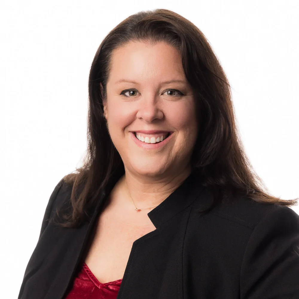 Studio headshot of a woman with dark hair in a black blazer on a white backdrop