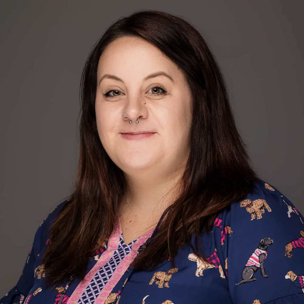Studio headshot of a woman with dark hair in a patterned navy top on a dark backdrop