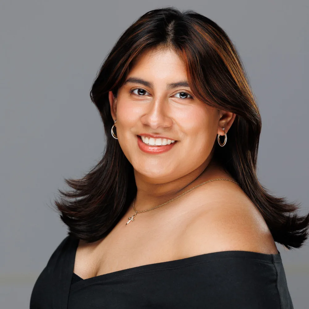 Studio headshot of a woman with dark hair in a black off-shoulder top on a gray backdrop