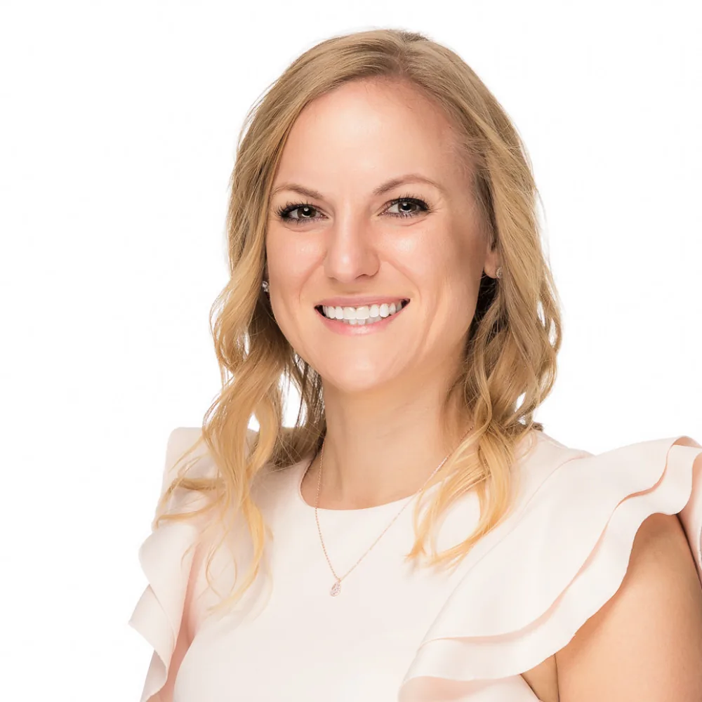 Studio headshot of a blonde woman in a cream ruffled top on a white backdrop