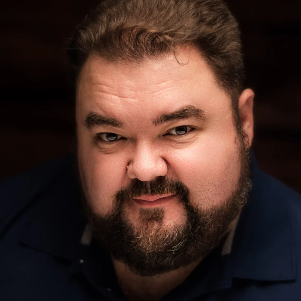 Studio headshot of a bearded man in a dark shirt on a dramatic dark backdrop