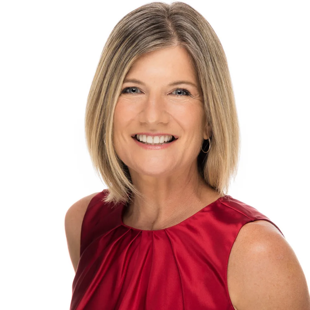 Studio headshot of a woman with a blonde bob in a red sleeveless top on a white backdrop