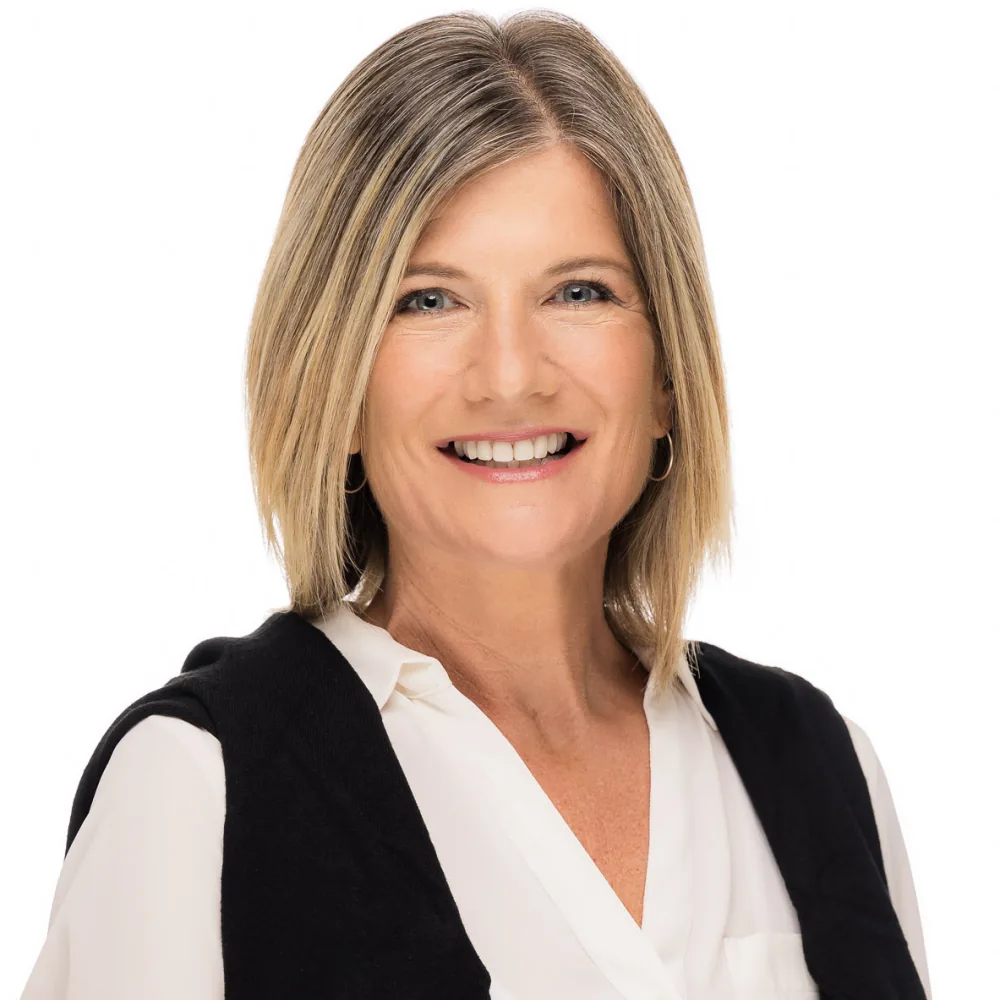 Studio headshot of a woman with blonde highlights in a black vest over white on a white backdrop
