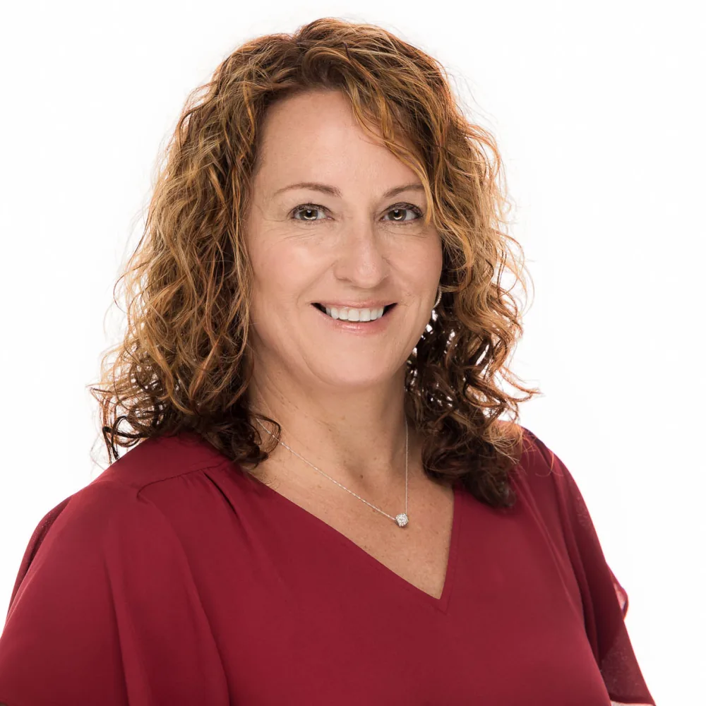 Studio headshot of a woman with curly auburn hair in a red top on a white backdrop