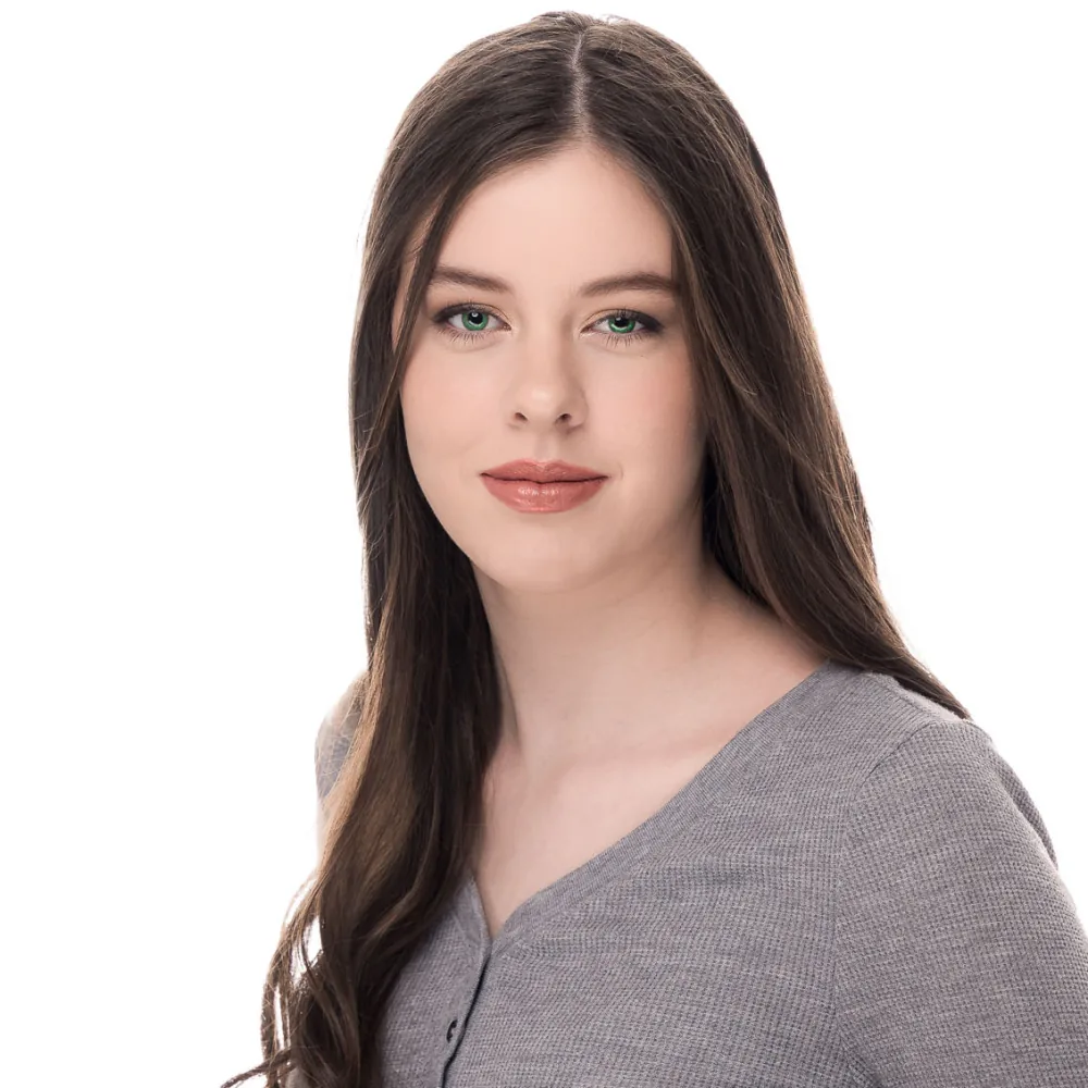 Studio headshot of a young woman with long dark hair in a gray top on a white backdrop