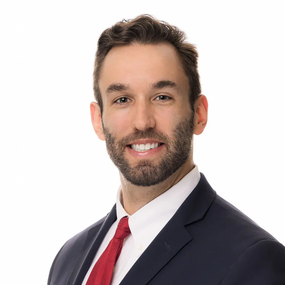 Executive headshot of a man with a beard in a navy suit and red tie on a white backdrop